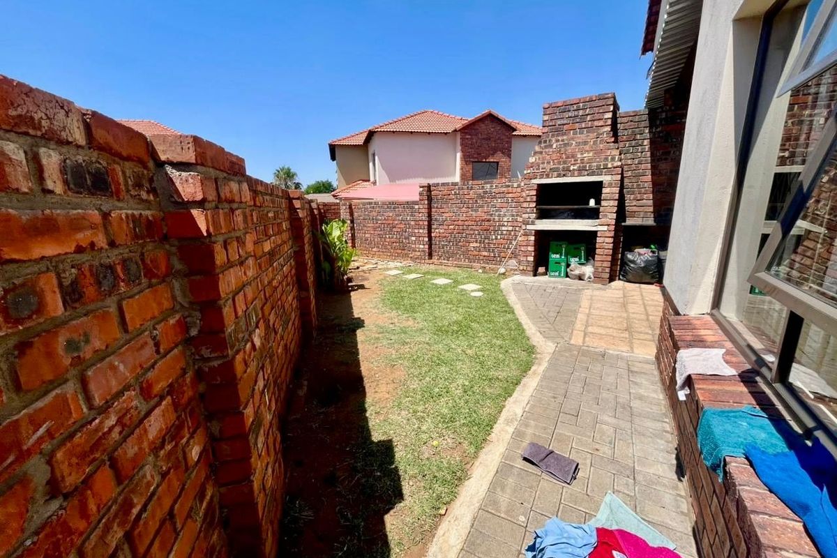 A private rear garden featuring a paved walkway, a built-in brick braai, and a brick boundary wall.