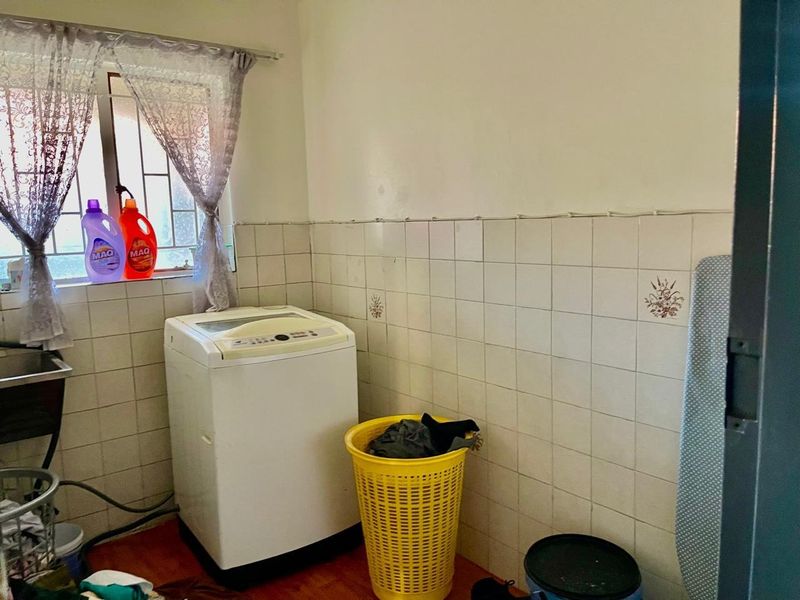 A functional laundry room featuring tiled splashbacks, a utility sink, and security bars on the window.