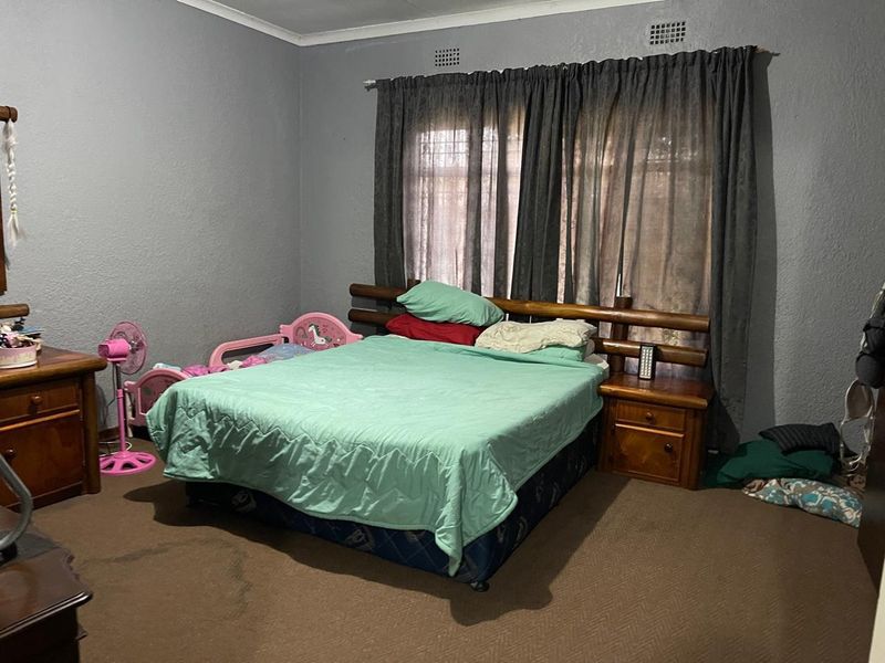 A standard bedroom featuring carpeted flooring, grey painted walls, and built-in ventilation grilles above the window area.