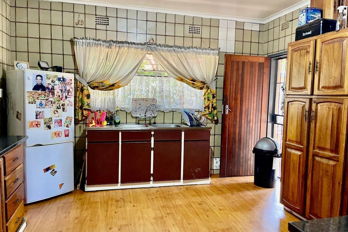 A dated kitchen featuring wooden cabinetry, a double sink, tiled backsplash, and laminate flooring, offering potential for modernization and renovation.