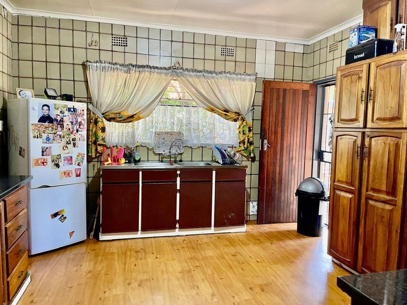A dated kitchen featuring wooden cabinetry, a double sink, tiled backsplash, and laminate flooring, offering potential for modernization and renovation.