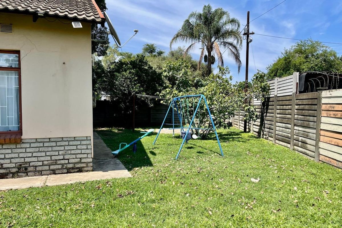 Rear garden area featuring a lawn, concrete boundary wall with security fencing, and a tiled roof structure with visible exterior wall plaster cracking.