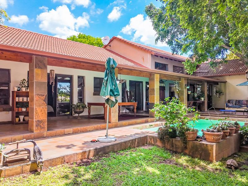 Spacious rear patio area featuring stone-clad pillars, tiled flooring, and direct access to a swimming pool and garden.