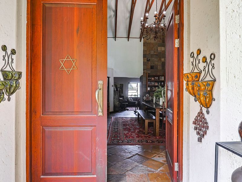 Inviting entrance featuring double timber doors, stone tile flooring, and a view into the living area with exposed ceiling beams and a stone fireplace.