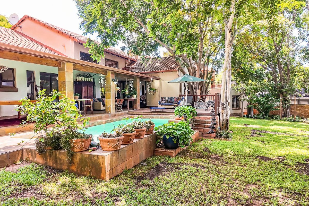 Rear view of the property featuring a swimming pool, covered patio, wooden deck, and established garden with mature trees.