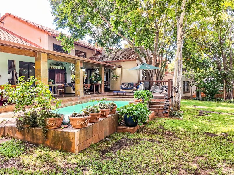 Rear view of the property featuring a swimming pool, covered patio, wooden deck, and established garden with mature trees.