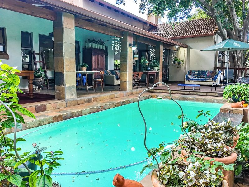 A spacious outdoor entertainment area featuring a swimming pool, covered patio with stone-clad pillars, and wooden decking, ideal for relaxed outdoor living.