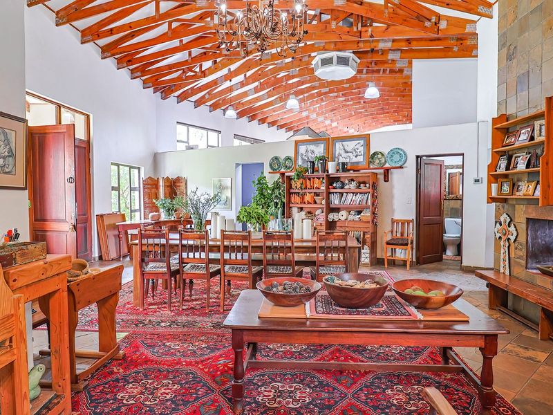 Spacious open-plan living and dining area featuring high exposed timber trusses, a prominent stone-clad fireplace, and traditional terracotta floor tiles.