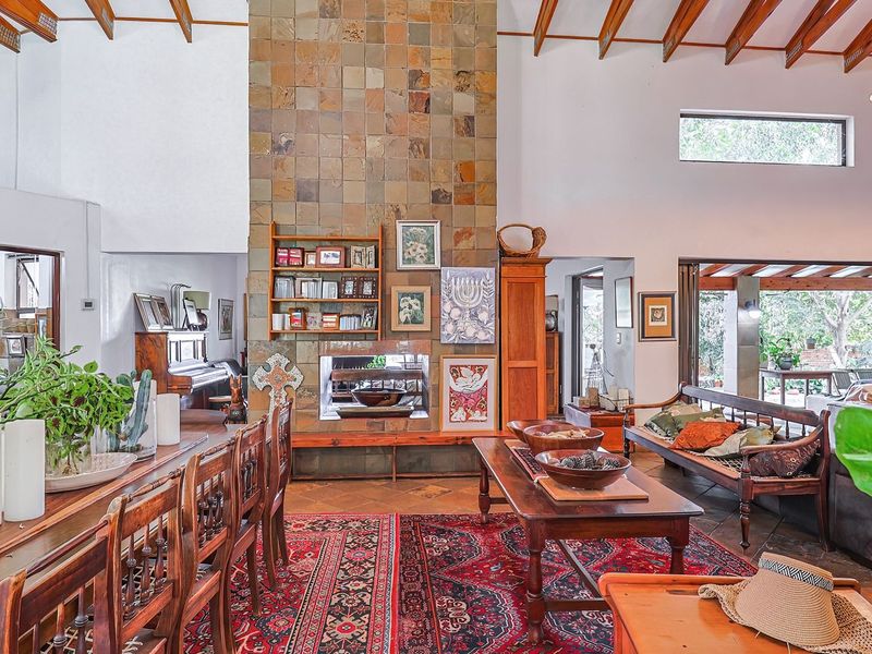 Spacious open-plan living and dining area featuring a prominent stone-tiled fireplace, exposed timber beams, and large stacking doors opening to the garden.