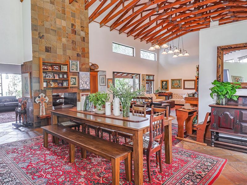 Spacious open-plan living and dining area featuring a striking stone-clad fireplace, vaulted ceilings with exposed timber rafters, and classic terracotta floor tiles.