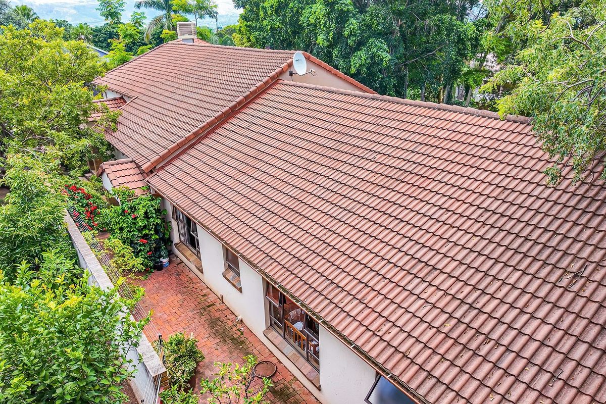 Aerial view of the property showing the terracotta tiled roof, brick paved patio area, and surrounding mature garden foliage.