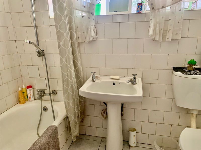 A functional bathroom featuring a pedestal basin, bathtub with shower mixer, and toilet, finished with white ceramic wall tiling.