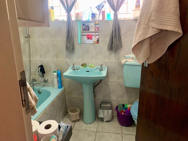 A dated bathroom featuring a blue pedestal basin, matching bathtub, and toilet with tiled walls and flooring.