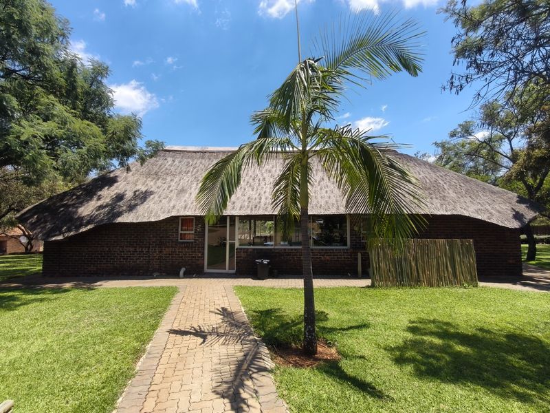Front view of a farm-style dwelling featuring a traditional thatch roof, face brick exterior, and a paved walkway leading to the entrance.