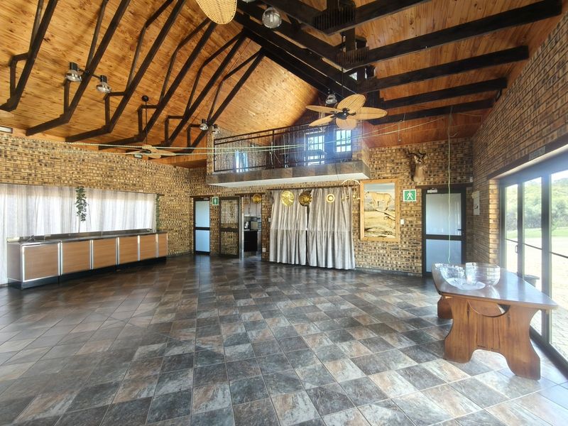 Spacious living area featuring high vaulted timber ceilings, exposed rafters, facebrick walls, and a mezzanine level with a metal balustrade.