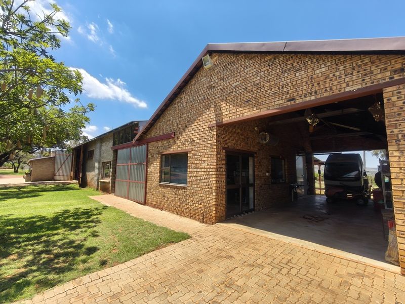 Rear view of a face brick farm building featuring a paved driveway and a large covered carport area.