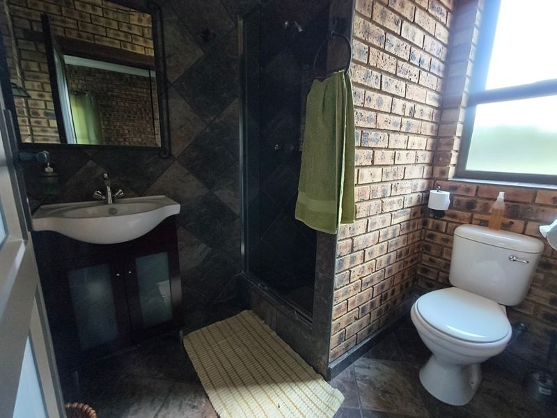 A bathroom featuring exposed brick walls, a vanity with a basin, a shower enclosure, and a toilet, finished with tiled flooring.