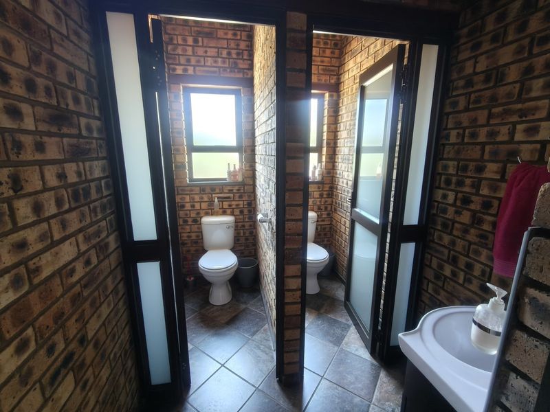 A functional bathroom featuring exposed brick walls, tiled flooring, a pedestal basin, and two separate toilet cubicles with frosted glass doors.