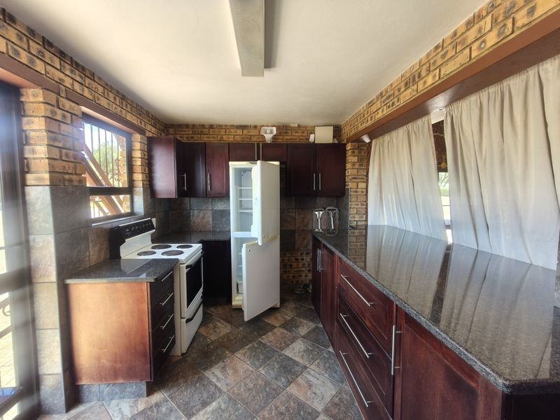 A rustic kitchen featuring exposed brick walls, dark wood cabinetry, granite countertops, and tiled flooring, offering a functional layout with ample workspace.