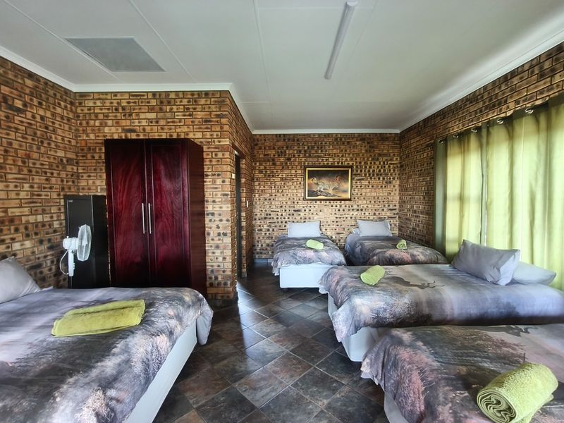 Spacious bedroom featuring exposed brick walls, tiled flooring, and a built-in cupboard, currently configured with multiple beds.