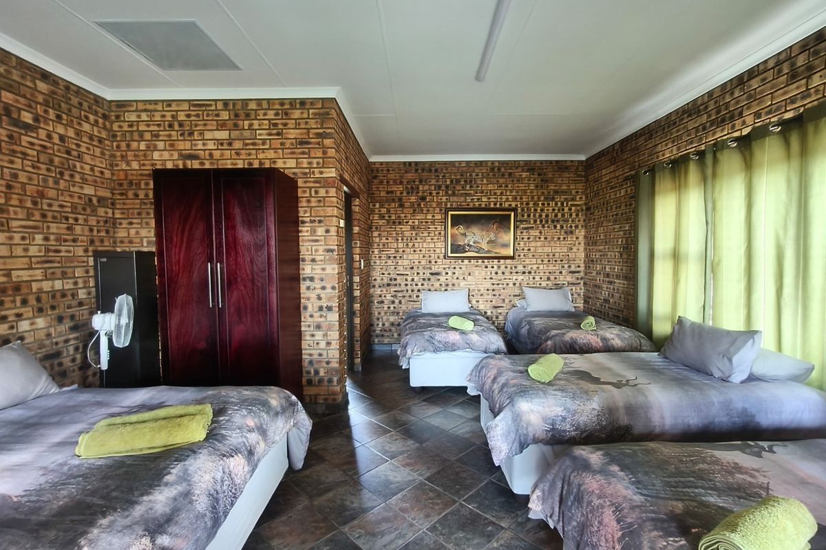 Spacious bedroom featuring exposed brick walls, tiled flooring, and a built-in cupboard, currently configured with multiple beds.