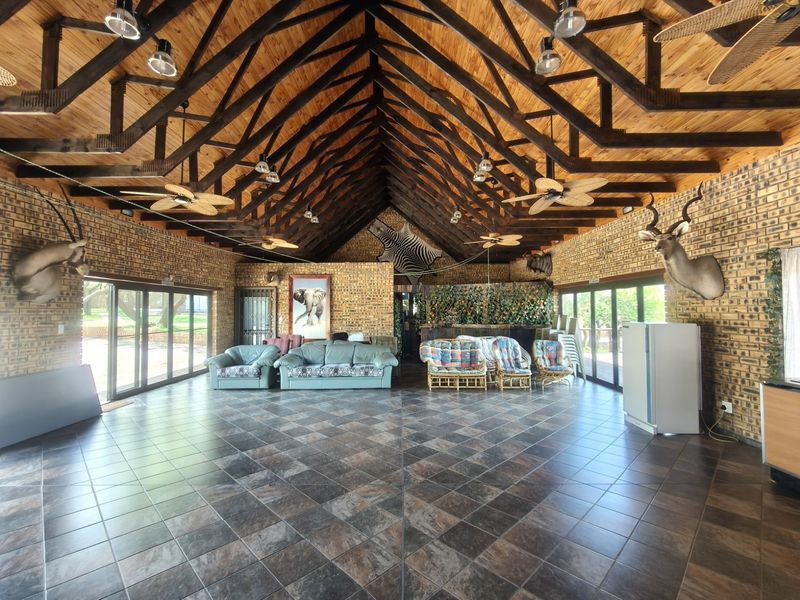 Spacious living area featuring high exposed timber roof trusses, exposed brick walls, tiled flooring, and large sliding glass doors providing ample natural light.