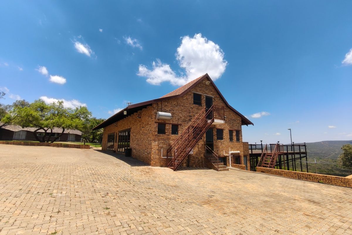 Rear view of a face brick farm building featuring an external metal staircase, a raised wooden deck, and a spacious paved driveway area.