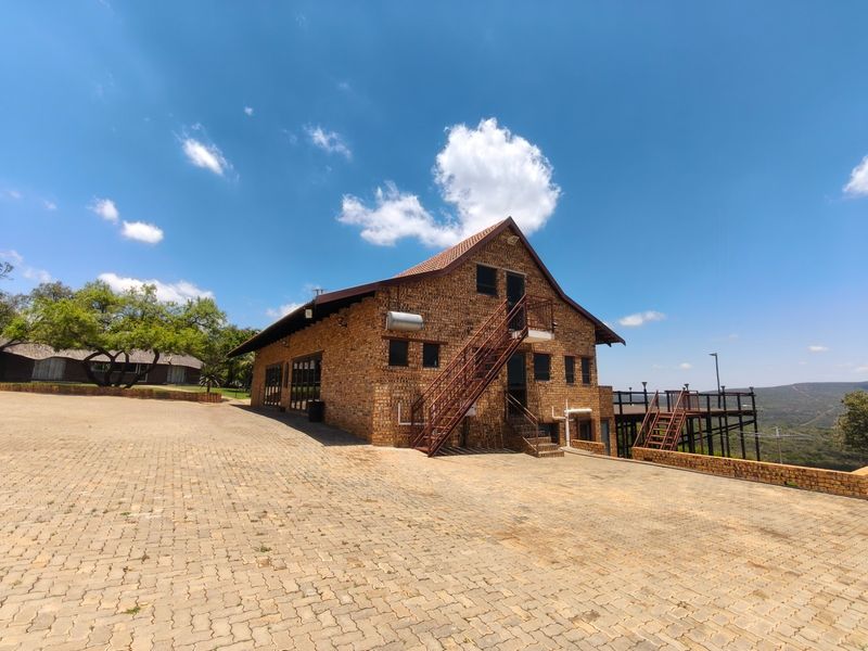 Rear view of a face brick farm building featuring an external metal staircase, a raised wooden deck, and a spacious paved driveway area.