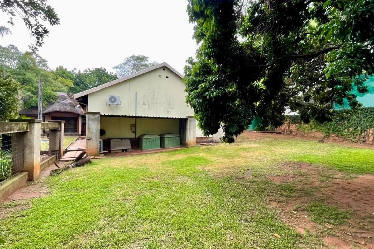 A view of the rear garden area featuring a lawn, concrete boundary wall, and the rear elevation of the property with an external air conditioning unit.