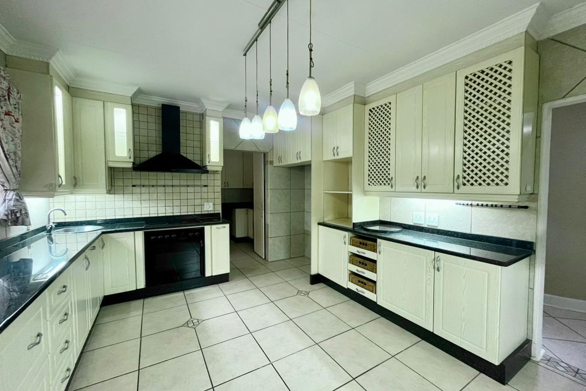 Spacious kitchen featuring cream cabinetry, dark granite countertops, tiled backsplash, built-in oven, extractor fan, and ceramic floor tiles.
