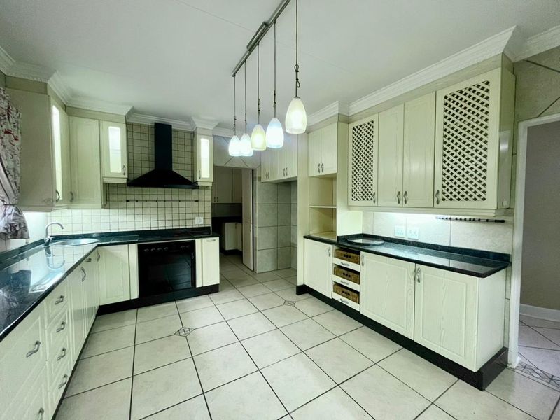 Spacious kitchen featuring cream cabinetry, dark granite countertops, tiled backsplash, built-in oven, extractor fan, and ceramic floor tiles.