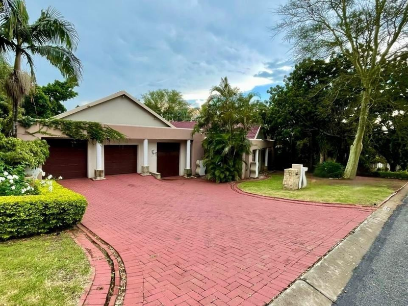 Front exterior view of the property featuring a triple garage, extensive paved driveway, and established landscaped garden.