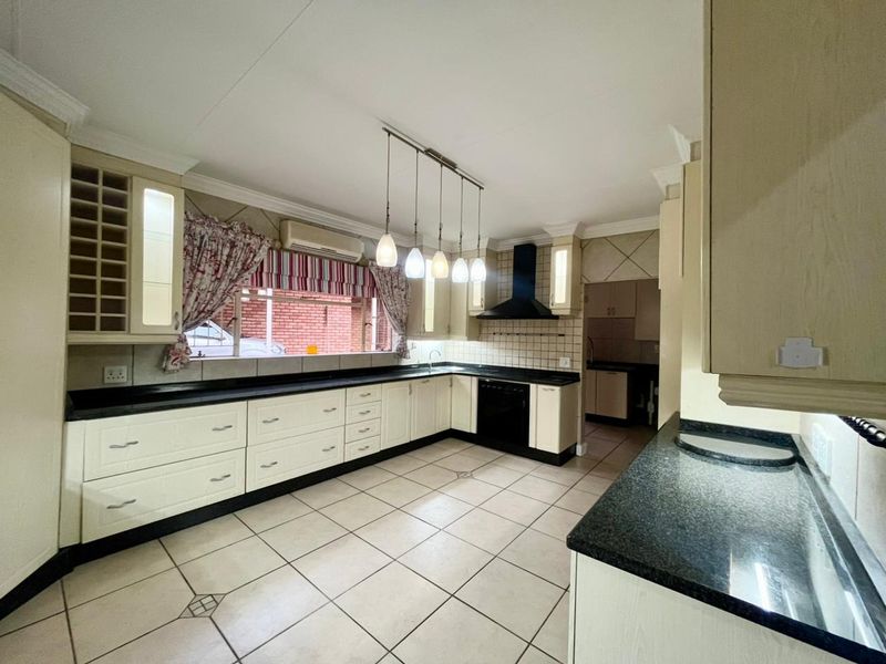Spacious kitchen featuring ample built-in cabinetry, granite countertops, tiled flooring, and an integrated extractor fan, with an adjacent scullery area.