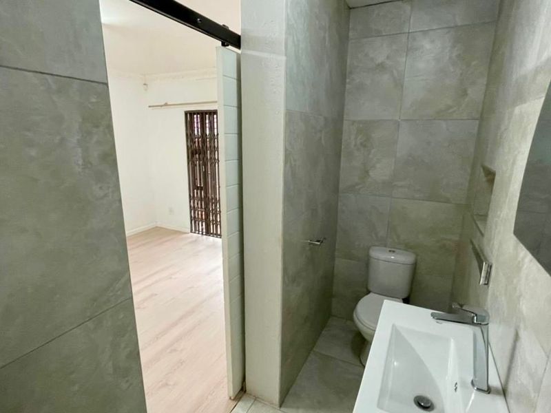 A modern bathroom featuring large format wall tiles, a wall-mounted vanity with chrome mixer tap, and a sliding barn door entrance.