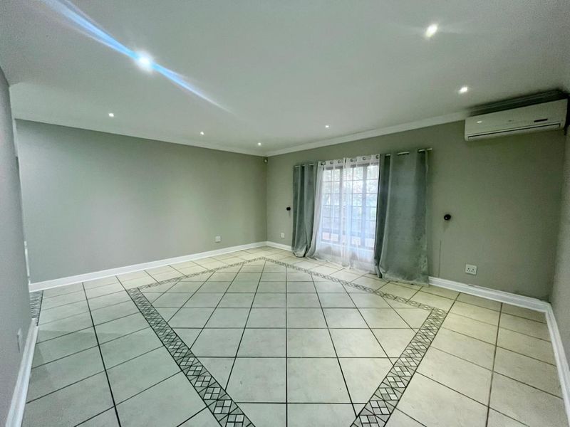 Spacious, light-filled living area featuring neutral wall tones, decorative tiled flooring, recessed lighting, and a wall-mounted air conditioning unit with direct patio access.