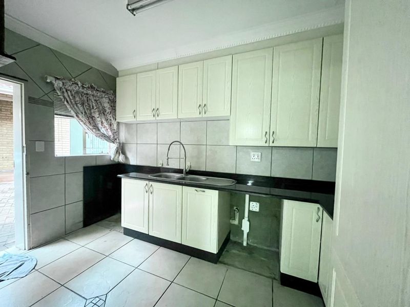 A functional scullery area featuring built-in cabinetry, granite countertops, a double basin sink, and tiled finishes, offering practical prep and wash-up space.