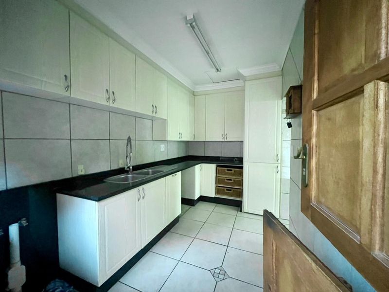 A functional kitchen featuring white built-in cabinetry, dark granite countertops, a double basin sink, and tiled flooring throughout.