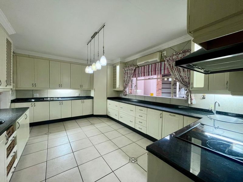 Spacious kitchen featuring extensive built-in cabinetry, granite countertops, integrated electric hob with extractor, and tiled flooring with ample workspace.
