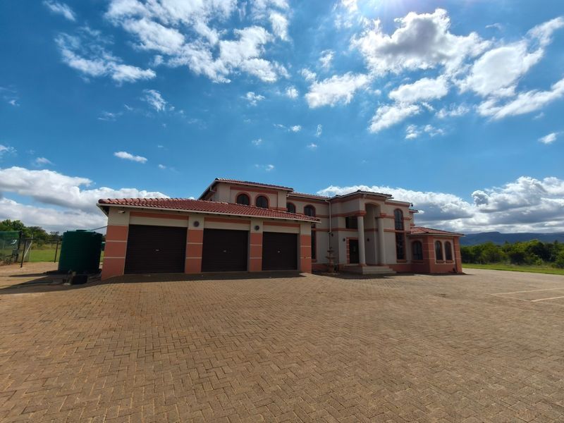 A spacious farm property featuring a large paved driveway, a triple garage, and a well-maintained exterior with a tiled roof and arched architectural details.