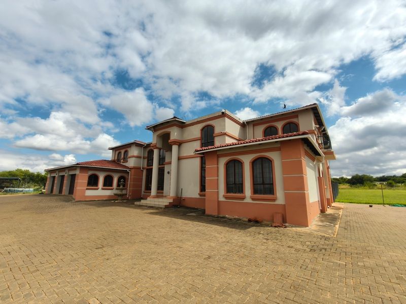 A large multi-story farm residence featuring arched windows, a paved driveway, and a multi-car garage under a terracotta tiled roof.