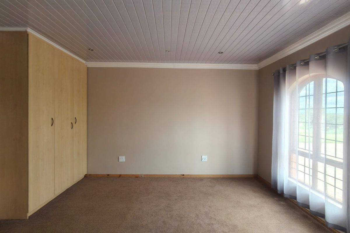 A spacious, empty bedroom featuring built-in cupboards, a tongue and groove ceiling with recessed lighting, and an arched window with natural light.