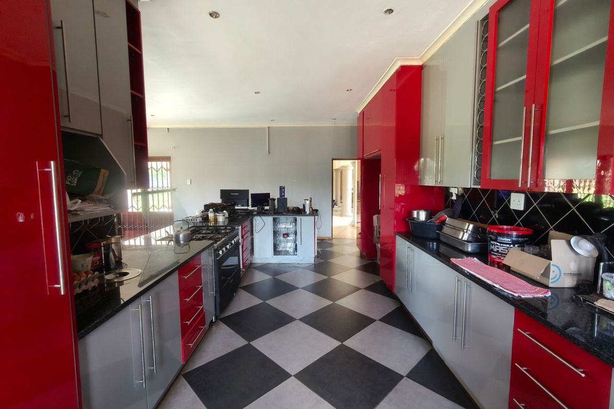 Spacious kitchen featuring high-gloss red and grey cabinetry, granite countertops, a gas hob, and a distinctive black and white checkered tiled floor.