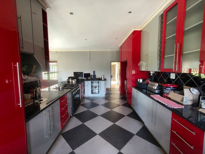 Spacious kitchen featuring high-gloss red and grey cabinetry, granite countertops, a gas hob, and a distinctive black and white checkered tiled floor.