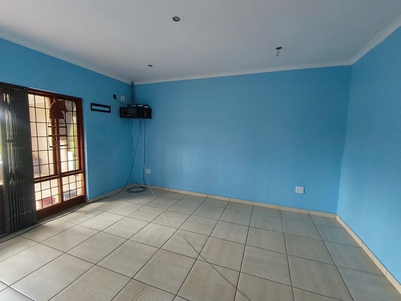 An empty living room featuring tiled flooring, recessed lighting, and a sliding glass door with a security gate.