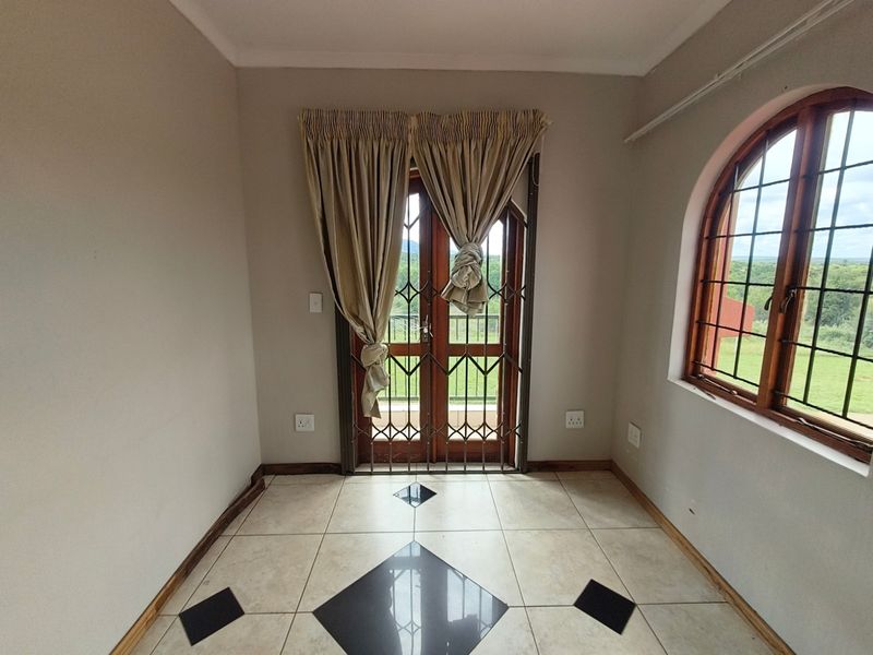 An empty living area featuring tiled floors with decorative inlays, an arched window, and double doors leading to an outdoor space with security gates.