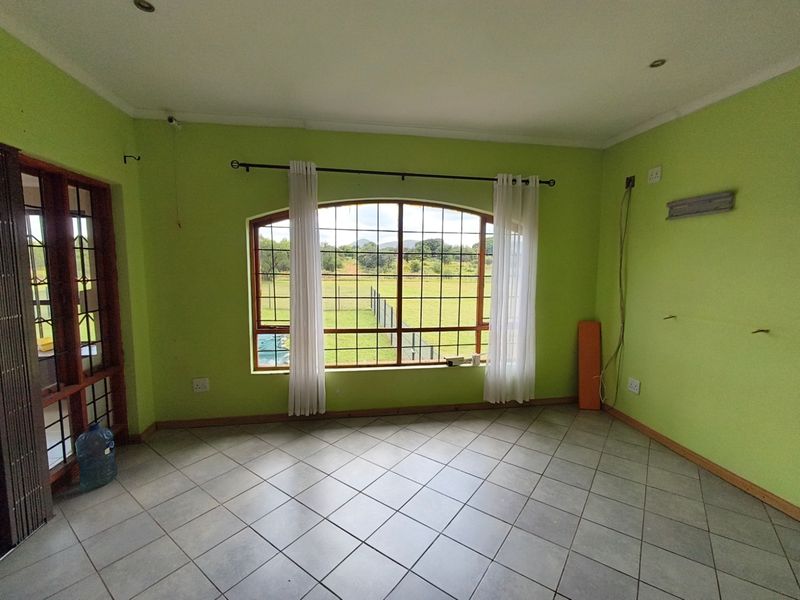 An empty living room featuring tiled flooring, recessed lighting, and an arch-top window with security bars, offering views of the surrounding farm landscape.