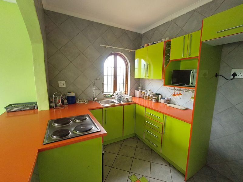 A functional kitchen featuring bright green cabinetry, orange countertops, an electric hob, and a tiled backsplash with a classic arched window.