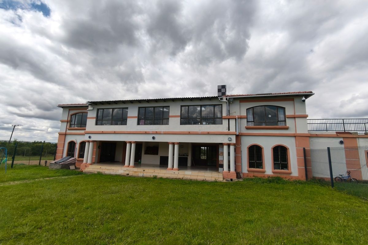 Rear view of a two-story farmhouse featuring a covered patio with columns, upper-level terrace, and expansive lawn area.