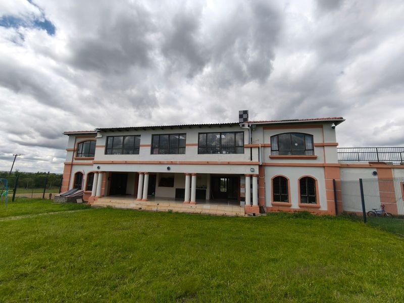Rear view of a two-story farmhouse featuring a covered patio with columns, upper-level terrace, and expansive lawn area.