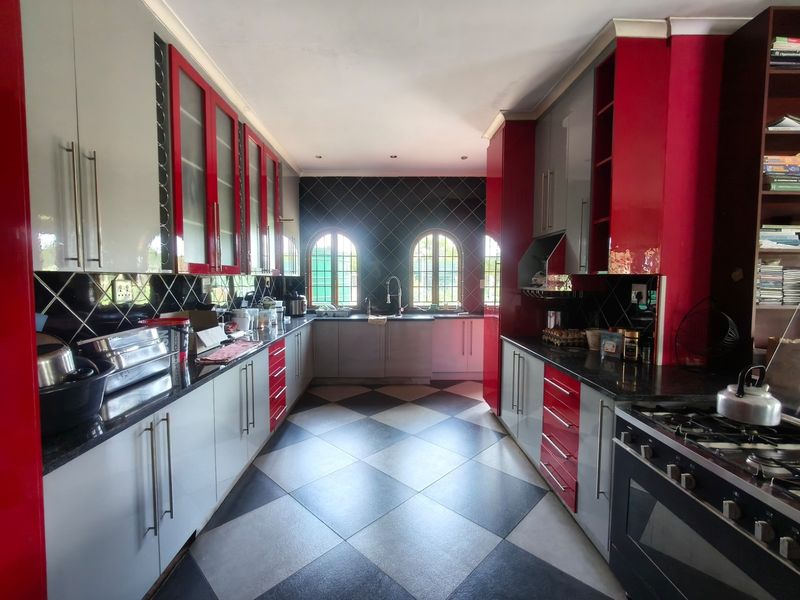Spacious kitchen featuring high-gloss red and grey cabinetry, granite countertops, a gas stove, and distinctive arched windows with a checkered tile floor.